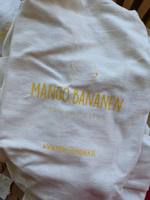 Ein Leinenstoff, auf dem "Mango.Bananen, Freude im Rucksack" steht.